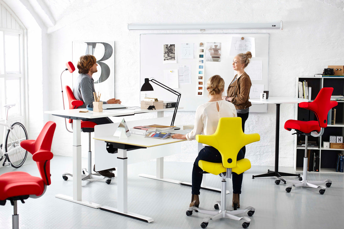 Modern office with people working at desks and colorful chairs.