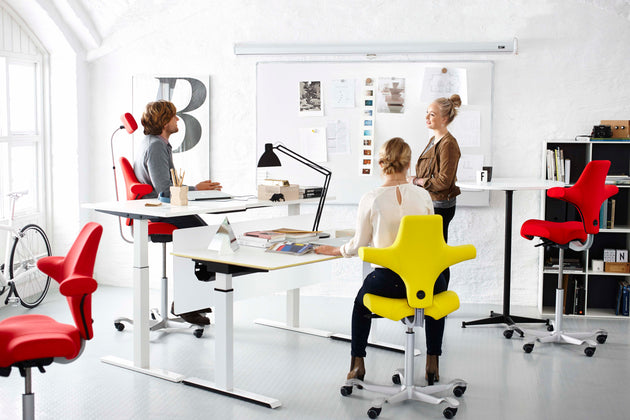 Modern office with people working at desks and colorful chairs.