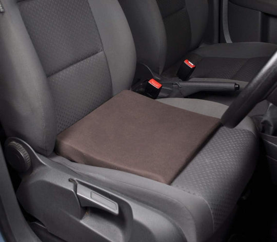 A black slimline wedge cushion placed on a car seat to demonstrate its use for posture support.