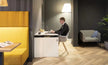 Person working on a laptop in a modern office setting with yellow booth seating and gray chair.