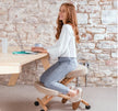 Woman sitting on a ergonomic kneeling chair at a desk with a stone wall background